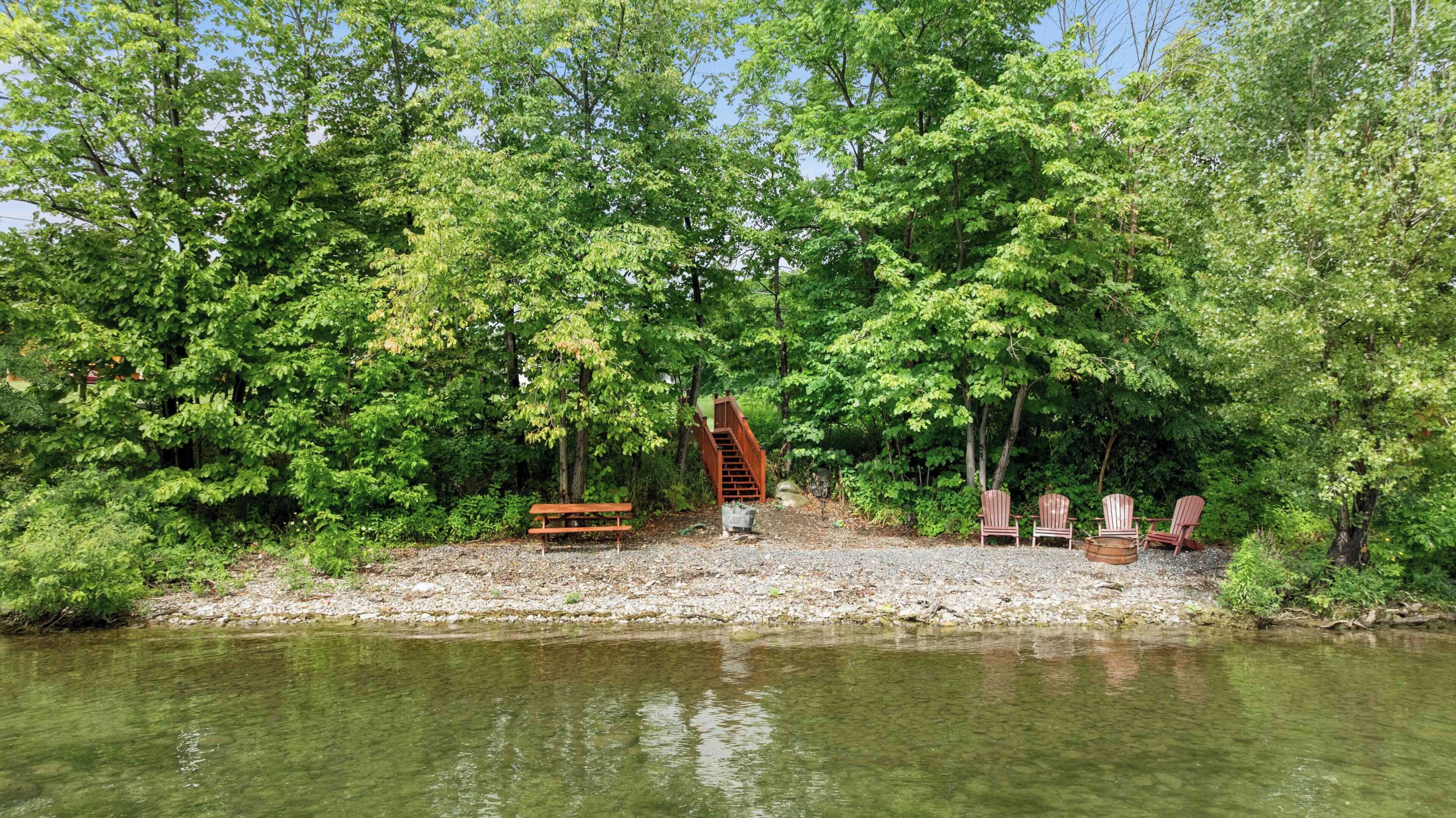 Une zone riveraine dotée d’un escalier en bois menant à une plateforme, le tout étant entouré d’arbres et agrémenté d’un banc.