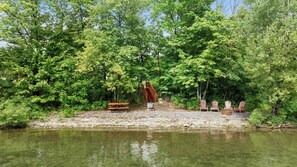 A riverside area with a wooden staircase leading up to a platform, surrounded by trees and a bench.