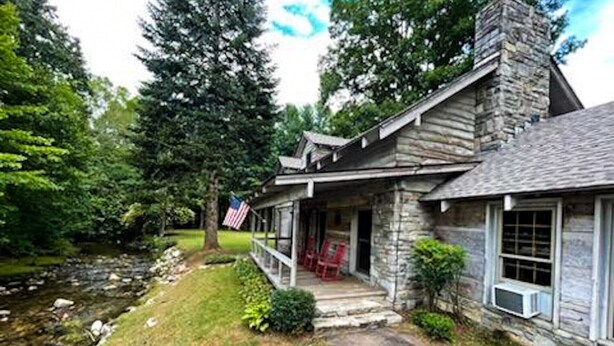 A stone house with a porch, a flag, and a small stream.
