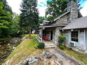 A stone house with a porch, a flag, and a small stream.