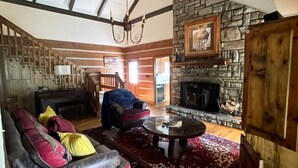 A spacious living room with a stone fireplace, wooden beams, and a large sofa with colorful cushions.