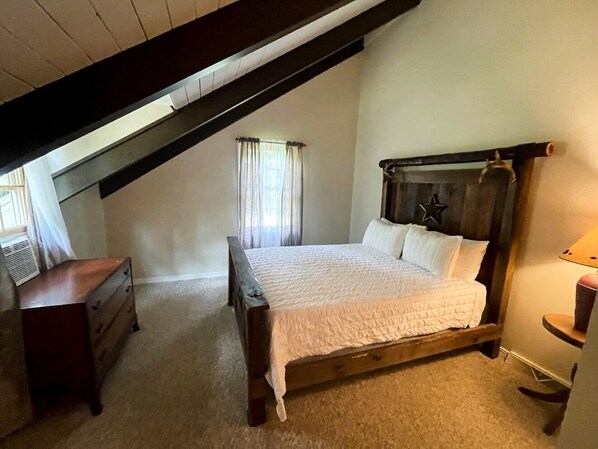 A bedroom with a sloped ceiling, a wooden bed with a star decoration, a dresser, and a lamp.