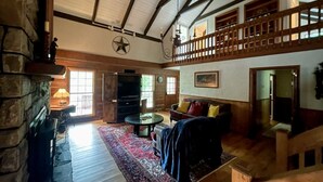 A spacious living room with a stone fireplace, a wooden staircase, and a large window.