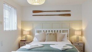 A neatly made bed with white linens, two bedside lamps, and a wooden paddle on the wall above the bed. - 2 bedroom accommodation in Sandgate (Sandgate)