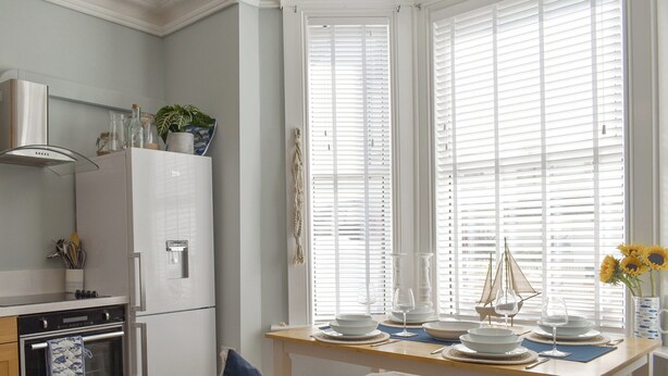 A modern kitchen with a refrigerator, oven, and a dining area with a table set for two. - 2 bedroom accommodation in Sandgate (Sandgate)