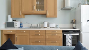 A compact kitchen with wooden cabinets, a microwave, a kettle, and a dishwasher. - 2 bedroom accommodation in Sandgate (Sandgate)