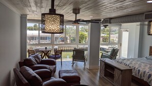 Une pièce spacieuse avec un plafond en bois, une grande fenêtre donnant sur une piscine, un canapé, un lit et un coin repas.