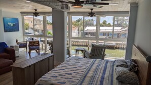 Une chambre avec un grand lit, un bureau et une chaise. Les fenêtres offrent une vue sur un port de plaisance et des palmiers.