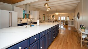 Une cuisine spacieuse dotée d’un grand îlot central, de meubles blancs et d’un plafond en bois.