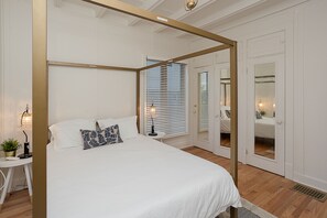 Un dormitorio con cama con dosel, una mesita de noche con lámpara y un espejo grande.