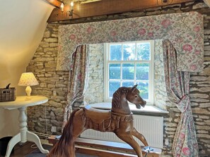 A room with a stone wall, a window with a view, a wooden horse sculpture, a table with a lamp, and floral curtains. - 3 bedroom accommodation in Hotham, near Beverley (Hotham, near Beverley)