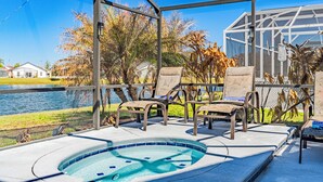 A pool area with lounge chairs, a hot tub, and a view of a lake and palm trees. - Be Our Guest (Kissimmee)