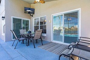 Un espace patio extérieur avec une table et des chaises, un téléviseur fixé au mur et de grandes fenêtres donnant sur une piscine.