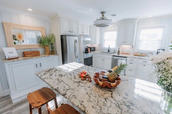 A modern kitchen with white cabinetry, a marble countertop, and a central island with a fruit bowl.