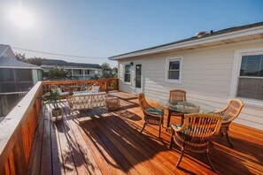 A wooden deck with wicker furniture and a glass table, overlooking a body of water.