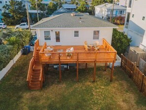 Ein eingeschossiges Haus mit einer Holzterrasse, einer kleinen Treppe und einem umzäunten Garten.