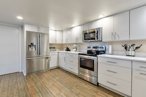A modern kitchen with stainless steel appliances, white cabinetry, and a wooden floor.