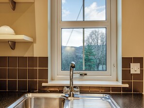 A kitchen with a stainless steel sink, a window with a view of trees and hills, and a white countertop.