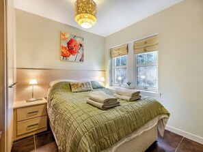 A bedroom with a bed, bedside lamps, a painting, and a window with blinds.