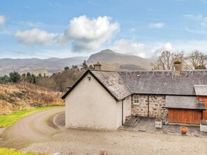 A rural house with a stone extension, a gravel driveway, and a mountain in the background.