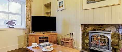 Un salón acogedor con televisor, chimenea y una mesa con tazas y pasteles.