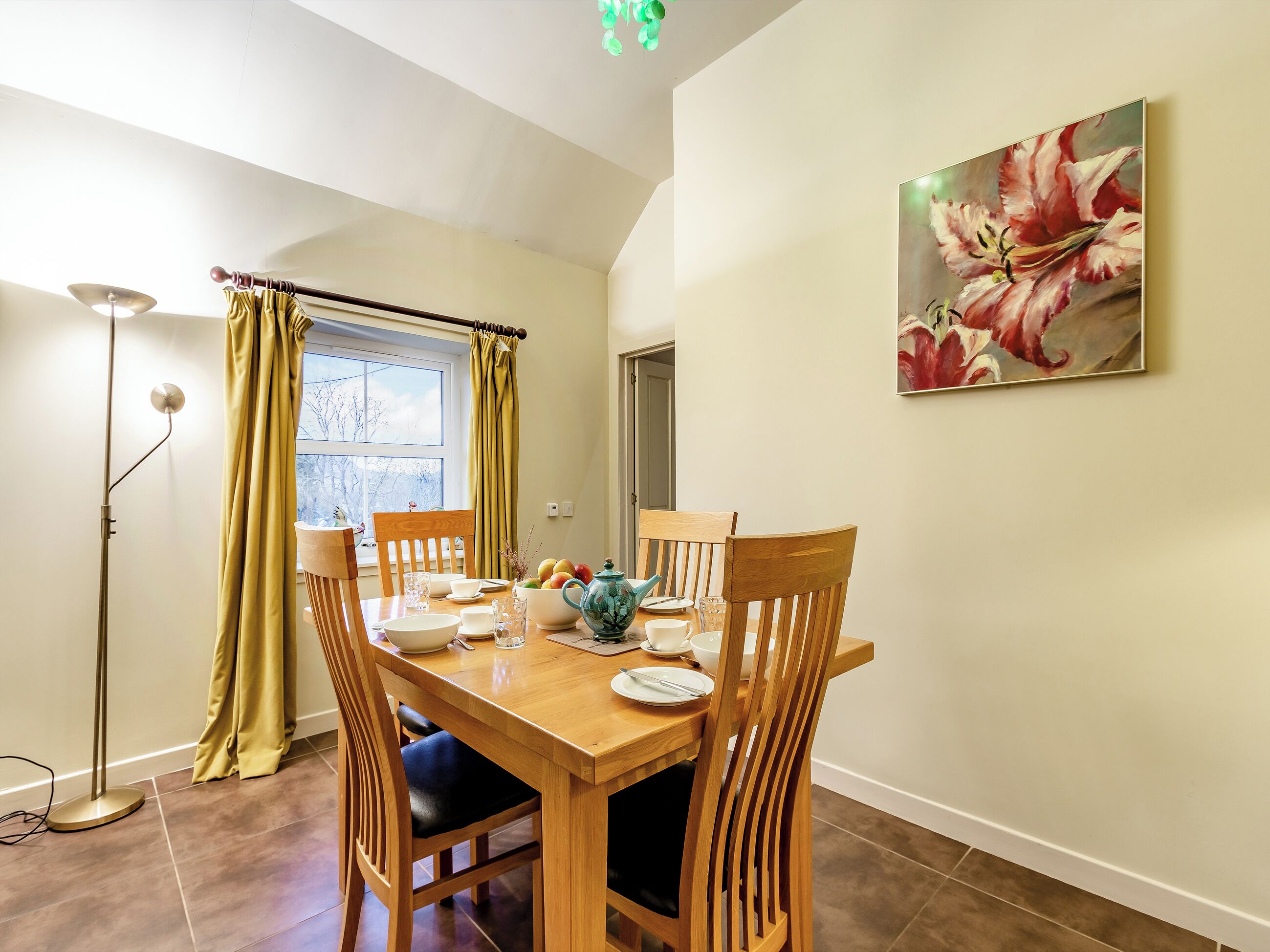 A dining area with a wooden table, chairs, and a painting of flowers on the wall.