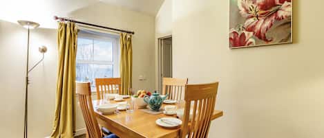 A dining area with a wooden table, chairs, and a painting of flowers on the wall.