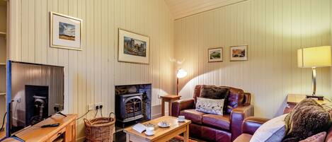 A cozy living room with a fireplace, leather sofa, wooden coffee table, and framed pictures on the wall.