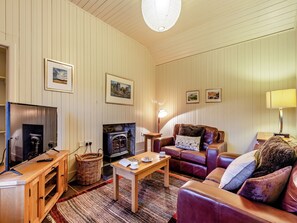 A cozy living room with a fireplace, leather sofa, wooden coffee table, and framed pictures on the wall.