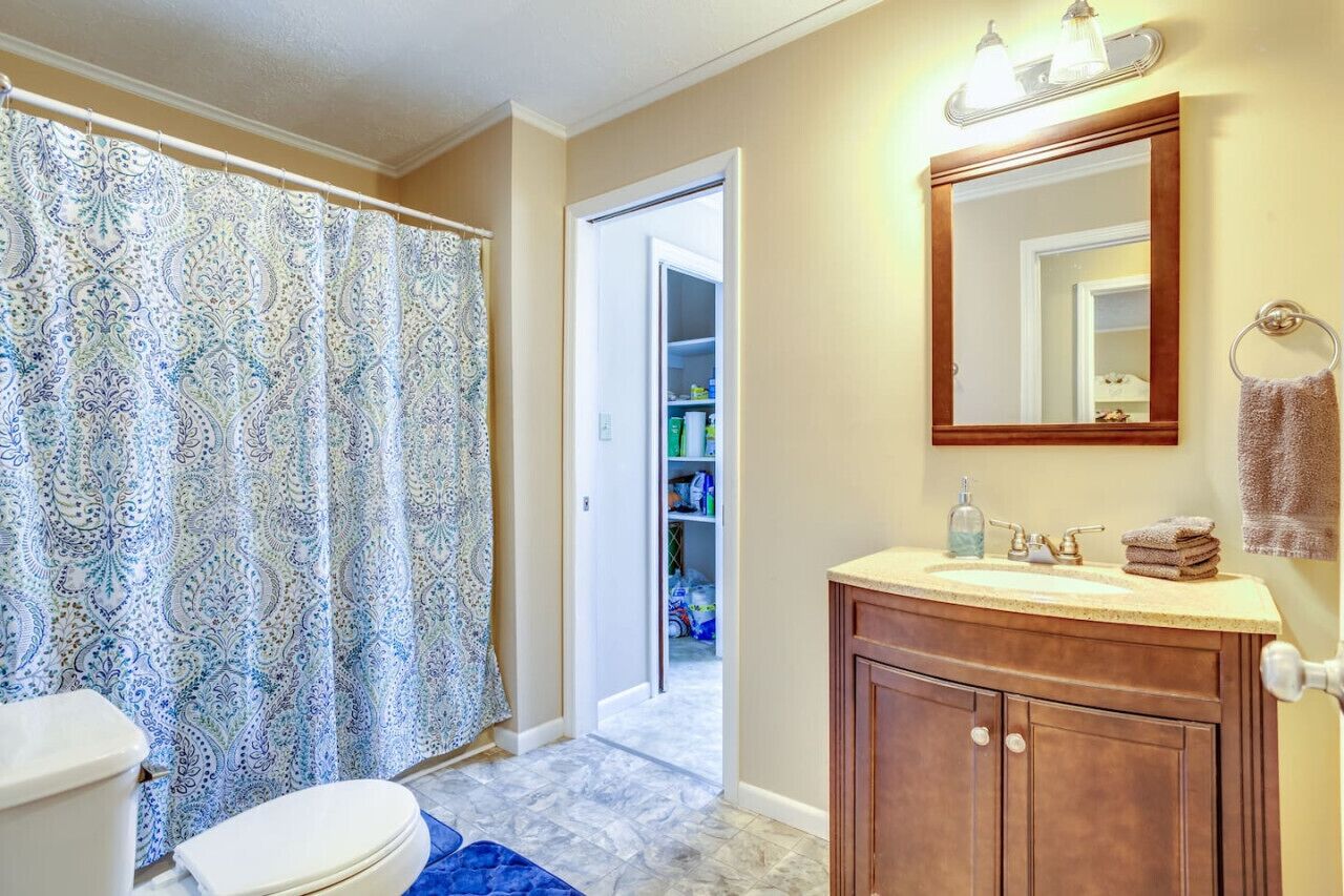 A bathroom with a toilet, shower curtain, vanity, and a mirror.