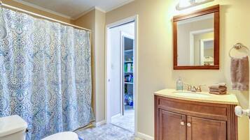 A bathroom with a toilet, shower curtain, vanity, and a mirror.