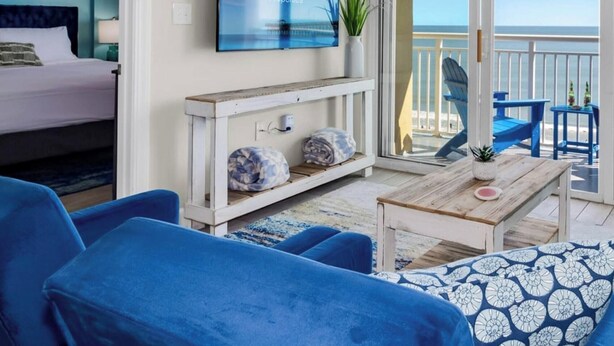 Una propiedad frente a la playa con balcón, una cama, muebles azules y televisor.