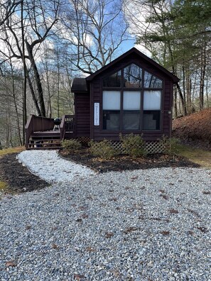 Eine Hütte mit einem 'Welcome'-Schild, einer Terrasse und einem Kiesweg, der dorthin führt.
