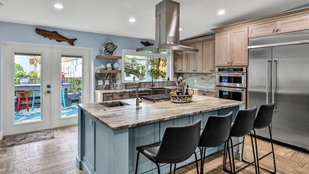 A modern kitchen with a large island, stainless steel appliances, and a view to the outside.
