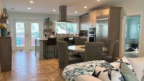 A modern kitchen with wooden cabinets, a central island, and a dining area with wicker chairs.