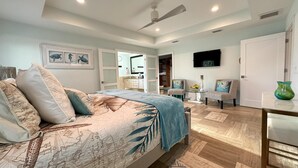 A bedroom with a bed, a desk, two chairs, a TV, and a bathroom visible through an open door.