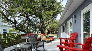A covered outdoor deck with seating, a table, and a house in the background.