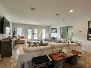 A spacious living room with a large white sofa, a wooden coffee table, and a dining area with a dark wooden table. - Spacious High Quality New Home - 1 Block to the Beach - 1 Pet Friendly (St. Augustine)