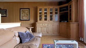 A cozy living room with a beige sofa, a glass coffee table, and wooden cabinets with glass doors. - Monte Solena 45C in Bormio (Bormio)