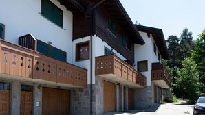 A multi-story building with wooden balconies, stone walls, and a car parked in front. - Monte Solena 45C in Bormio (Bormio)