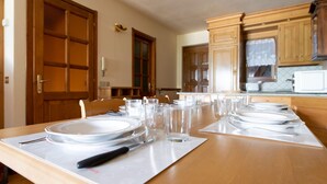 A dining table set for multiple people with chairs, a kitchen area with wooden cabinets, and a microwave. - Monte Solena 45C in Bormio (Bormio)