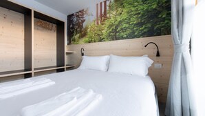 A hotel room with a bed, white linens, a wooden headboard, a wall-mounted lamp, and a large forest mural. - Italianway - San Pietro 8 - F - Pino - So-l563-spie8fs (Valdisotto)