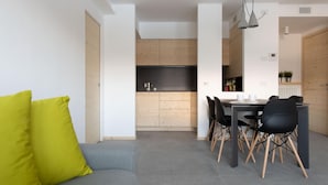 A modern living room with a grey sofa and a bright yellow pillow, leading to a dining area with a black table and chairs. - Italianway - San Pietro 8 - F - Pino - So-l563-spie8fs (Valdisotto)