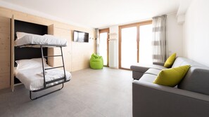 A compact room with a bunk bed, a green bean bag, a grey sofa with yellow cushions, and a TV on the wall. - Italianway - San Pietro 8 - F - Pino - So-l563-spie8fs (Valdisotto)