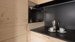 A modern kitchen with wooden cabinetry, a black countertop, a stainless steel coffee maker, and two white cups. - Italianway - San Pietro 8 - F - Pino - So-l563-spie8fs (Valdisotto)