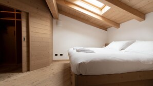 Un dormitorio con techo de madera, tragaluz, cama con ropa blanca y armario de madera.
