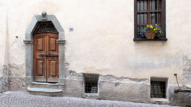 Un edificio con una puerta de madera grande, una ventana pequeña con una maceta de flores y el número '39' en la pared.