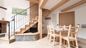 Una escalera de madera con un rellano de piedra, un área de comedor con sillas y mesa de madera, y un radiador en la pared.
