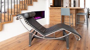 Uma sala de estar moderna com uma poltrona reclinável de couro preto, uma escada de madeira e uma área de cozinha.