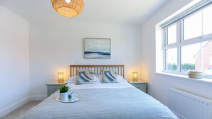 A bedroom with a large bed, bedside lamps, a window with a view, and a painting on the wall. - Elements 3 bed Home in Bracklesham Bay (Chichester)